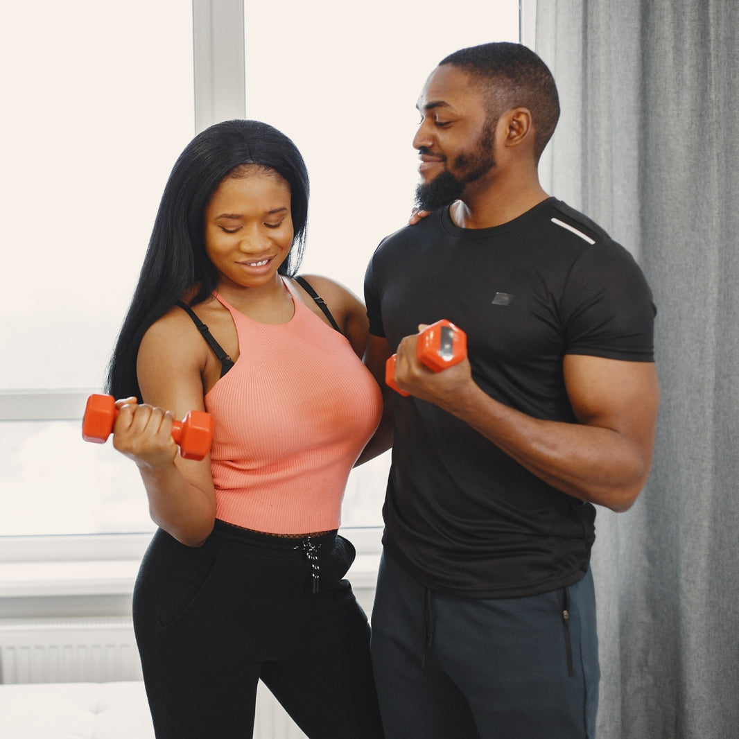A fit couple holding dumbbells while training together in gym.